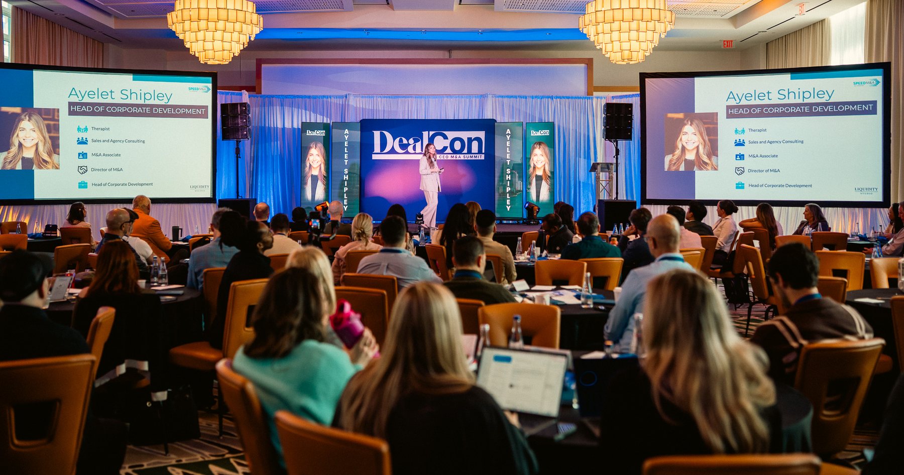Ayelet Shipley on stage at DealCon, with the audience in the foreground